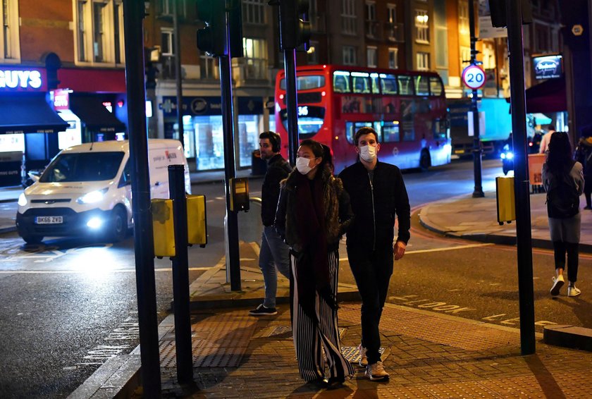 A couple wearing face masks walk down Clapham High Street in London