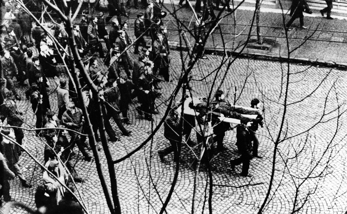 Gdynia. 17 grudnia 1970 roku. Ulicą Świętojańską demonstranci niosą na drzwiach zwłoki Zbigniewa Godlewskiego, który zginął w okolicy przystanku Szybkiej Kolei Miejskiej Gdynia Stocznia, przeszyty serią z karabinu maszynowego
