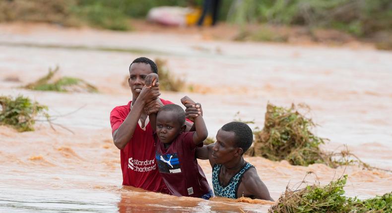 Residents help a young child while trying to cross a road damaged by El Nio rains on November 25, 2023.Brian Inganga/AP