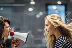 Profile view of angry female manager yelling at her colleague through megaphone.