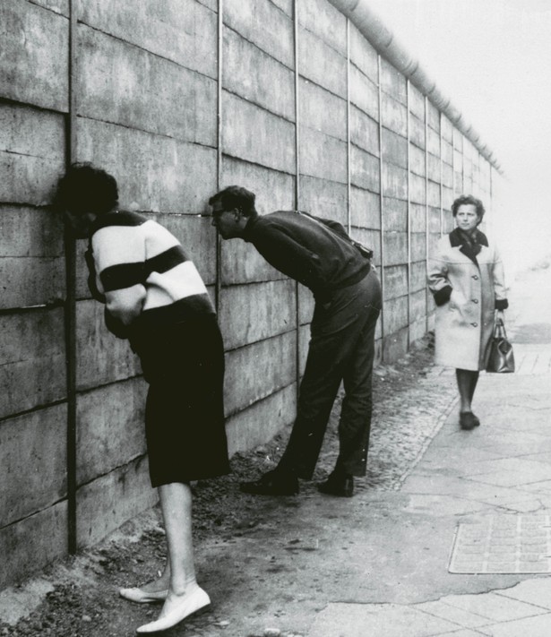 Mieszkańcy Berlina Zachodniego patrzą przez szpary w murze na wschodnią część miasta, 1966 r.