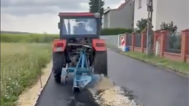 Poľský traktorista orie čerstvo položenú asfaltovú vozovku