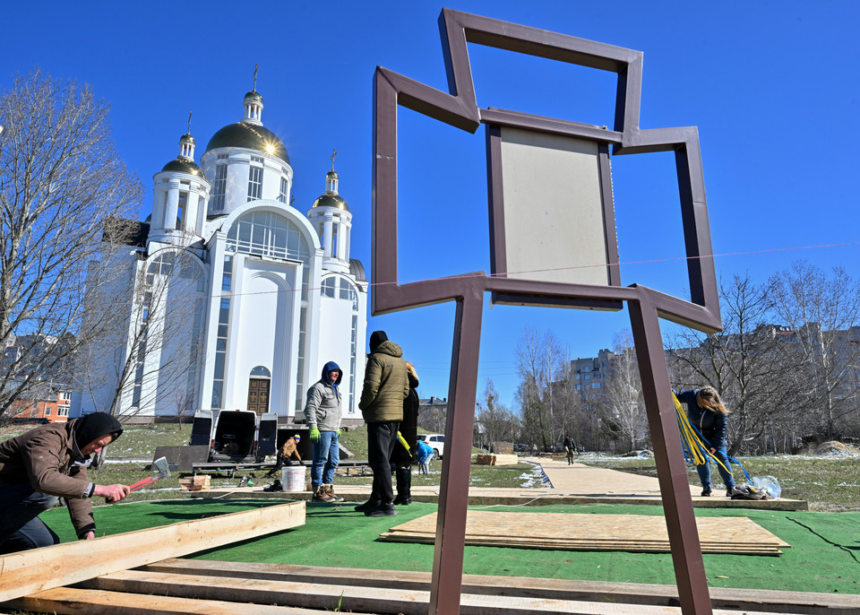 Robotnicy komunalni odnawiający teren przy symbolicznym krzyżu ustawionym na miejscu masowego grobu przy cerkwi pw. św. Andrzeja w Buczy (30 marca 2023 r.)