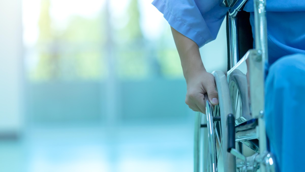 Asian disabled man is sitting in a wheelchair. He holds his hands on the wheel. Nearby are his colleagues, Medical equipment.