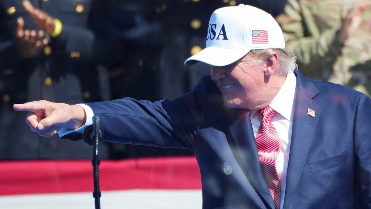 Americký prezident Donald Trump gestikuluje za ochranným sklom.