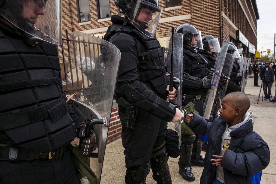 A young boy greets police officers in riot gear during a march in Baltimore on May 1, 2015, following the decision to charge six Baltimore police officers — including one with murder — in connection with the death of Freddie Gray, a black man who was arrested and suffered a fatal neck injury while riding in a moving police van.