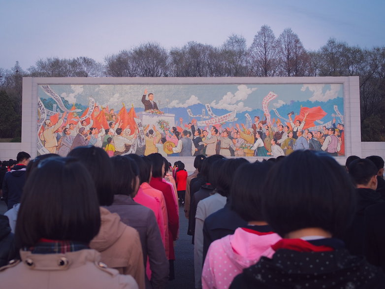 Dzieci stojące w rzędzie przed muralem w Pjongjangu 