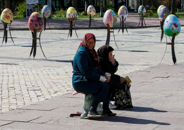 Elderly women beg for money near traditional Ukrainian Easter eggs Pysanky, displayed at square, a