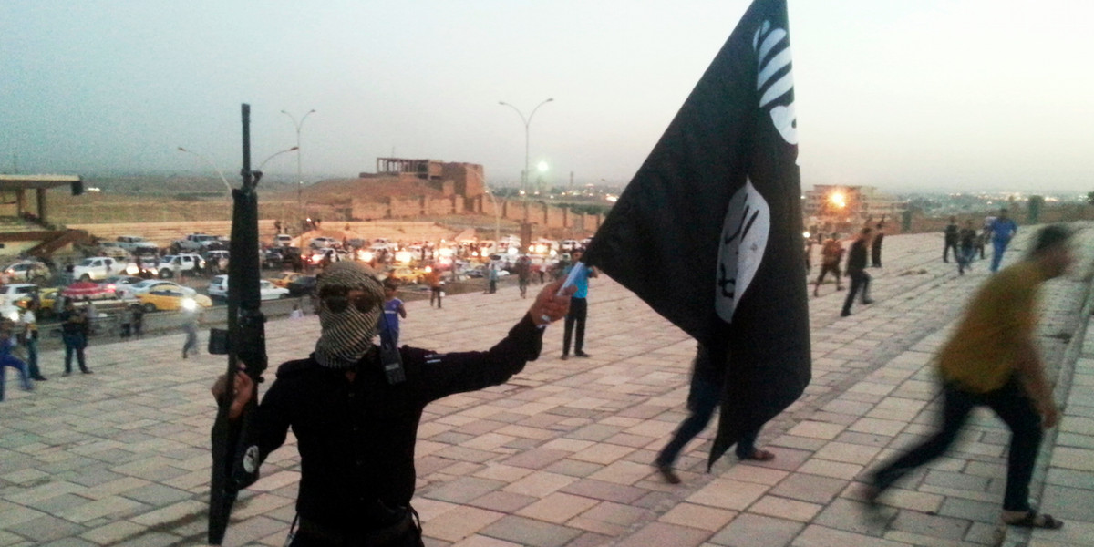 A fighter of the Islamic State of Iraq and the Levant (ISIL) holds an ISIL flag and a weapon on a street in the city of Mosul, June 23, 2014.