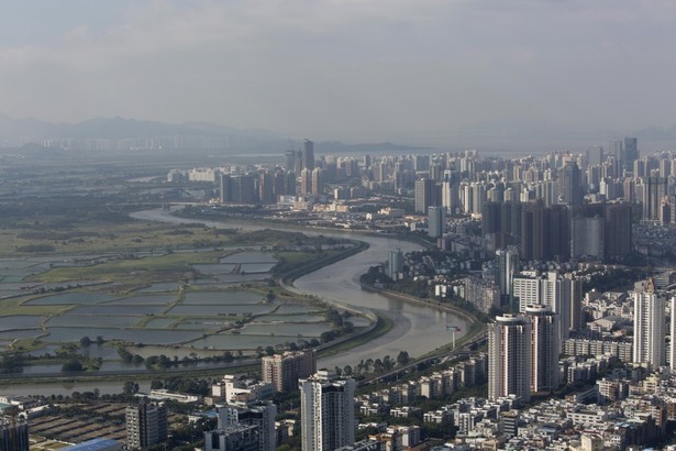 Gdy w 1977 roku Deng Xiaoping odwiedzał Shenzhen, była to tylko niewielka wioska rybacka, która funkcjonowała dzięki bliskości Hong Kongu, z którym graniczyła przez rzekę. Dostrzegając przepaść dzielącą warunki życiowe ówczesnej brytyjskiej kolonii i chińskiej osady, zdecydował o utworzeniu w Shenzhen specjalnej strefy ekonomicznej, która powstała w maju 1980 roku jako pierwszy tego typu obszar w Chińskiej Republice Ludowej. Po prawej stronie widzimy na zdjęciu budynki leżące w dzielnicy Luohu, sąsiadujące przez rzekę z obszarami uprawnymi należącymi do Hong Kongu.