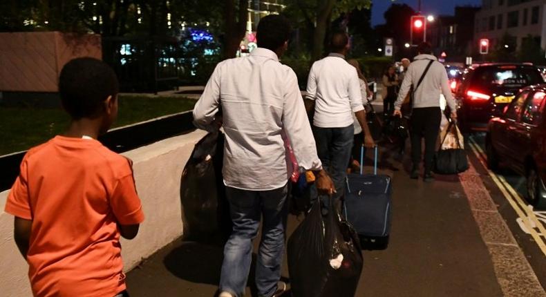 Residents walk with luggage and possessions as they evacuate from the Taplow Tower residential block on the Chalcots Estate in north London on June 23, 2017 because of fire safety concerns