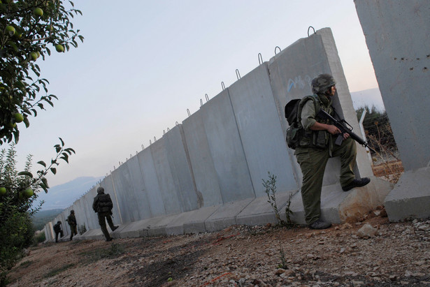 Izraelscy żołnierze kryją się za betonowym murem na granicy z Libanem w Metulah, fot. Nir Kafri/Bloomberg News