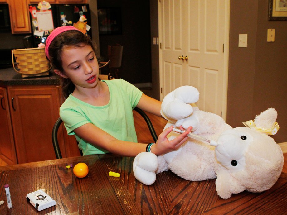 A girl practices injecting naloxone into her stuffed lamb.