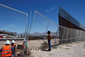 File photo of a boy looking at U.S. workers building a section of the U.S.-Mexico border wall at Sun