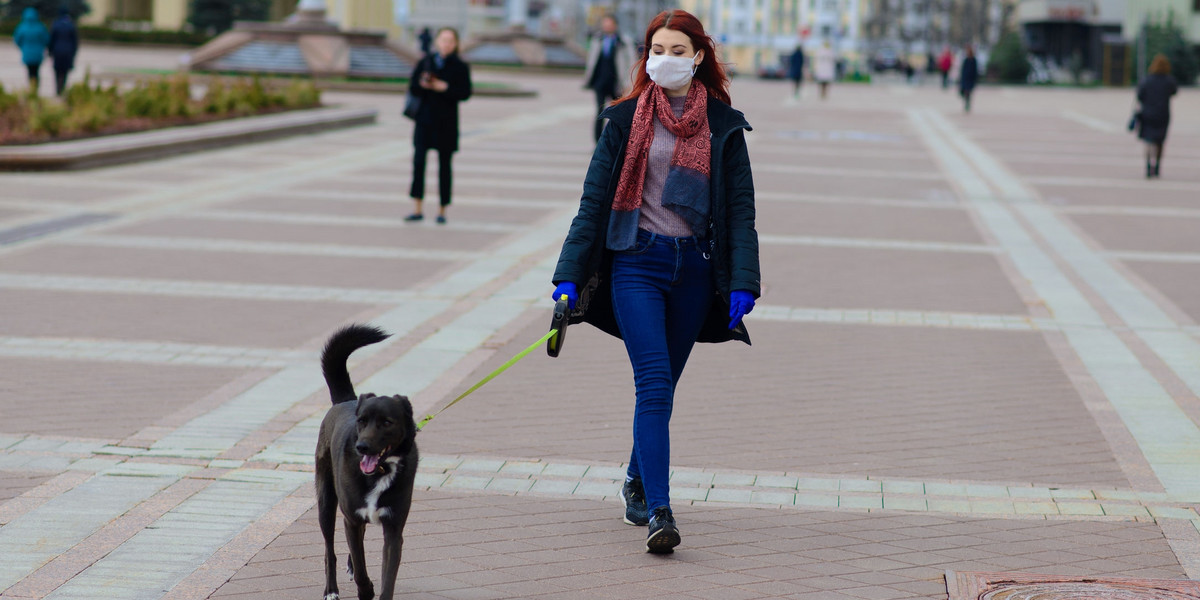 Young female using a face mask as a coronavirus spreading prevention walking with her dog. Global CO