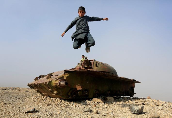 An Afghan boy jumps from the remains of a Soviet-era tank on the outskirts of Jalalabad