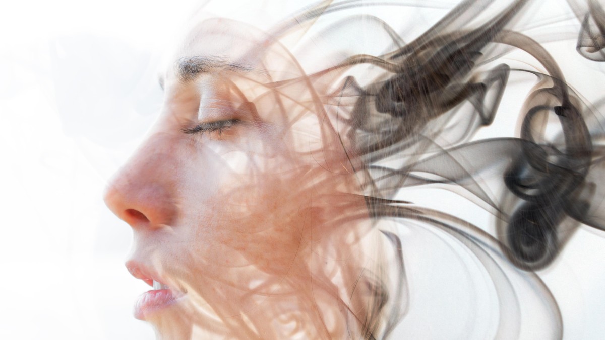 Double exposure portrait of a young fair-skinned woman and a smoky texture dissolving into her facial features