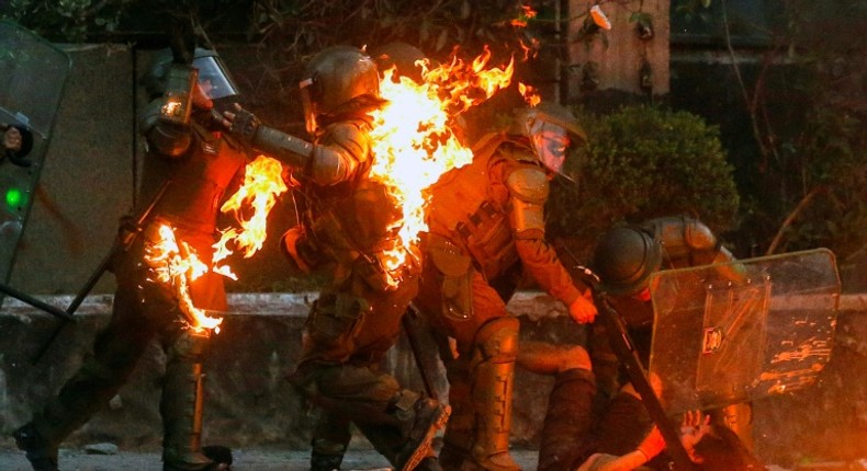 A demonstrator is held while a petrol bomb hits riot police during a protest against the government in Santiago on Friday