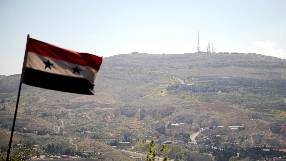 A Syrian national flag flutters as Qasioun mountain is seen in the background from Damascus