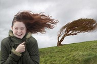 Young woman standing on windswept hill, smiling, eyes closed