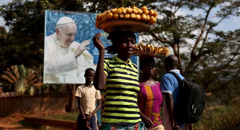 Women carrying fruits and vegetables on their heads walk past a billboard with a photograph of Pope Francis, in Bangui, Central African Republic, November 26, 2015. REUTERS/Siegfried Modola