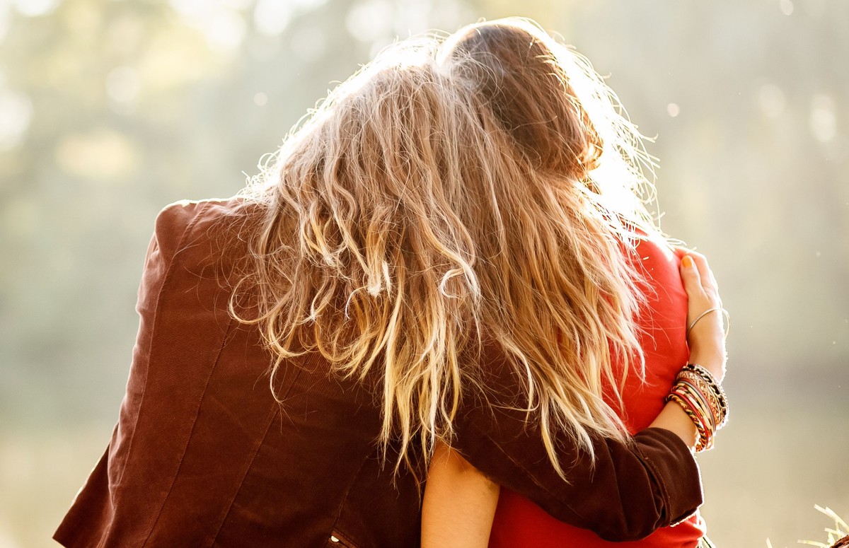 Two,Young,Women,Sitting,On,Grass,Hugging,Rear,View