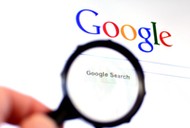 Hand holds Magnifying glass against Google homepage