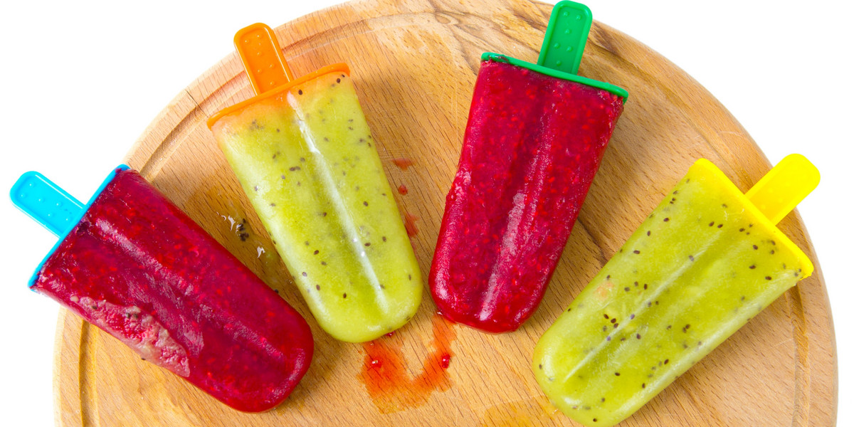 Homemade popsicle with lime juice, kiwi fruit and raspberry against wooden background.