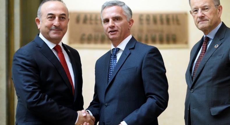 Turkey's Foreign Minister Mevlut Cavusoglu (L) shakes hands with Swiss sounterpart Didier Burkhalter (C) as Director General of the UN Office in Geneva Michael Moller looks at UN headquarters in the Swiss city on January 12, 2017