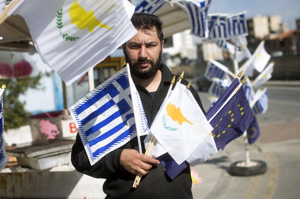 Sprzedawca flag w stolicy Cypru Nikozji pozuje do zdjęcia z flagami Cypru, Grecji oraz Unii Europejskiej.