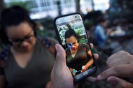 A Pokemon appears on the screen next to a woman as a man plays the augmented reality mobile game Pokemon Go by Nintendo in Bryant Park in New York City