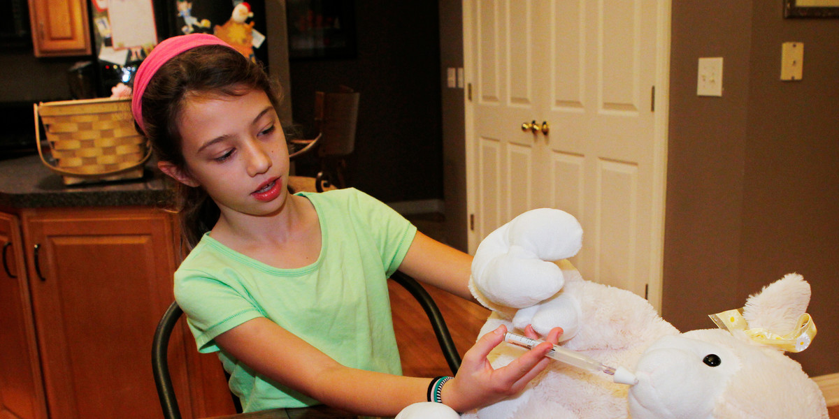 A girl practices injecting naloxone into her stuffed lamb.