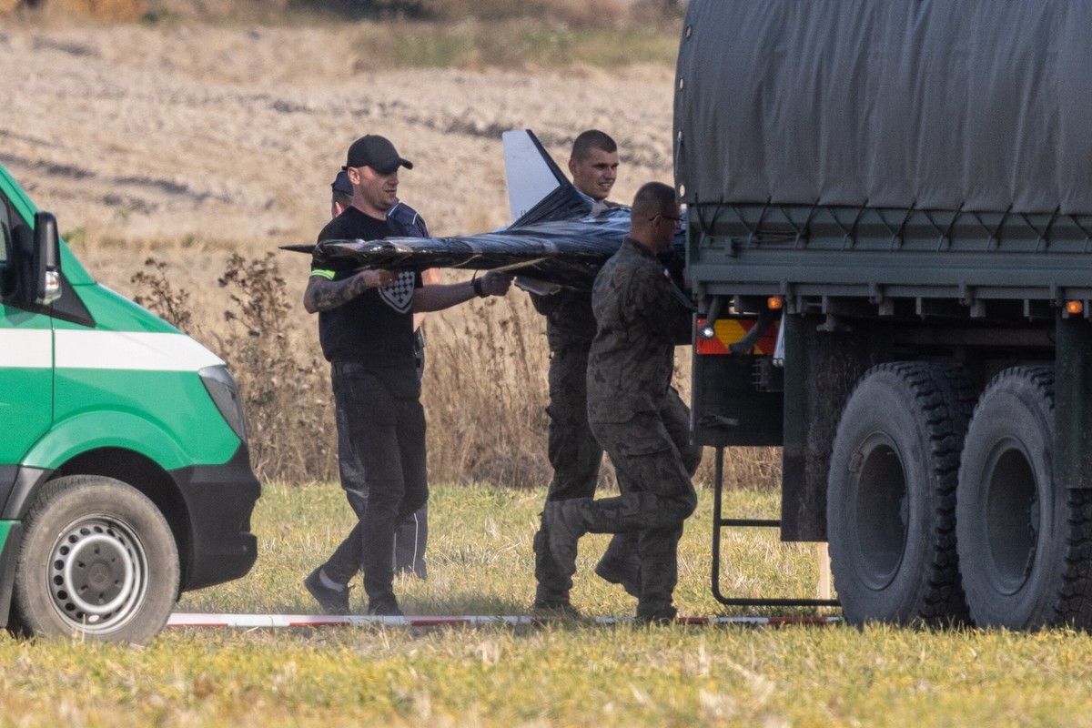 Żołnierze i funkcjonariusze ładują do wojskowej ciężarówki szczątki zestrzelonego drona, akcja odbywa się na polu, obok stoi zielony pojazd służb.