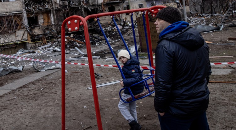 Ukrán apa gyermekével a lebombázott házuk előtt.