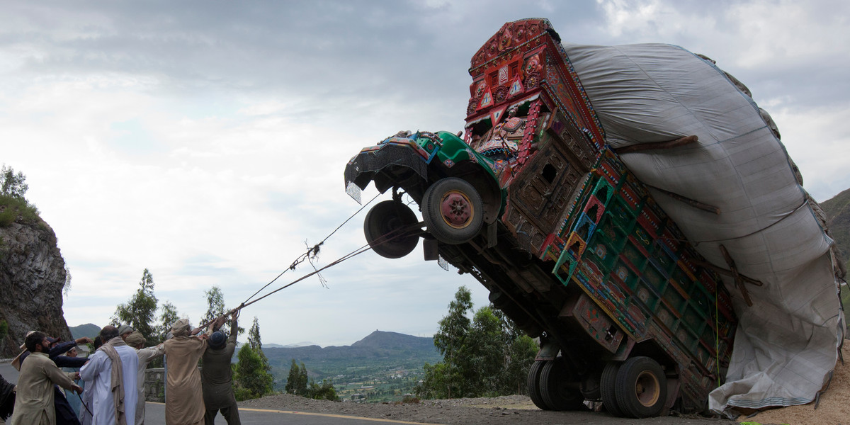 Men trying to right an overloaded supply truck along a road in Dargai.