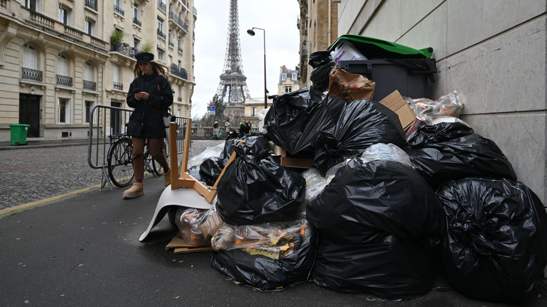 Kobieta przechodzi obok pojemników na śmieci przepełnionych śmieciami na ulicach podczas strajku śmieciarzy w Paryżu, Francja, 13 marca 2023 r.