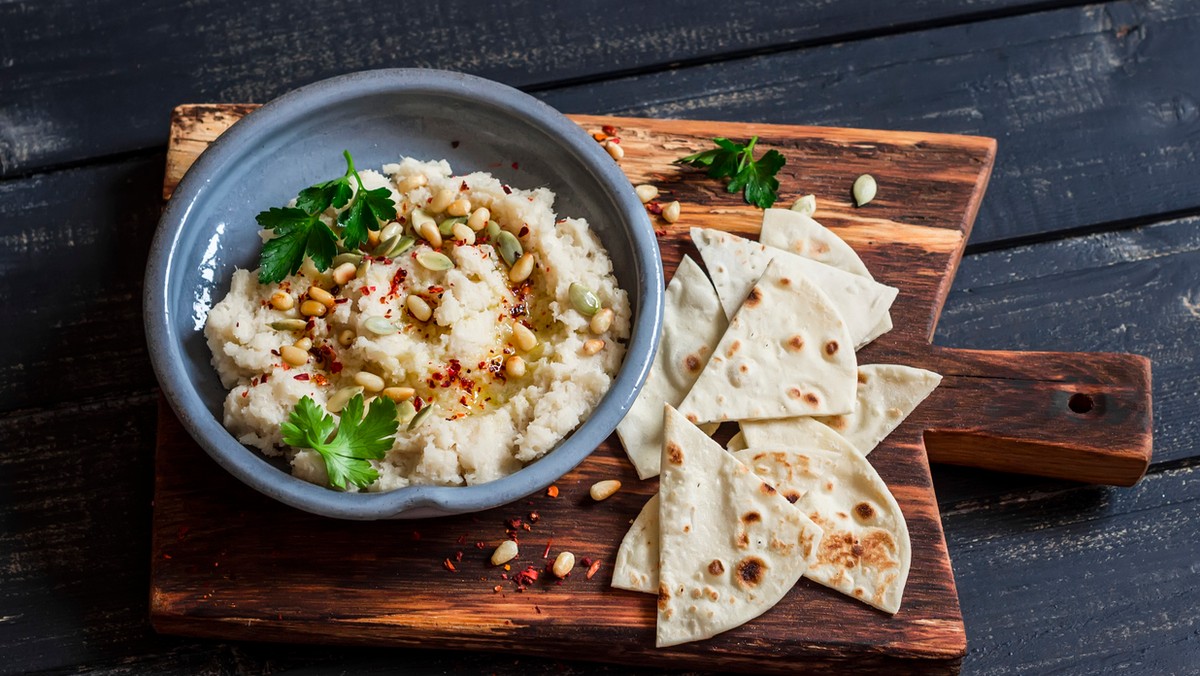 Hummus to popularna arabska potrawa, która doskonale smakuje do kanapek, a także jako składnik sałatek. Mało kto potrafi jednak zrobić tego typu pastę z ciecierzycy w taki sposób, aby nie tylko dobrze smakowała, lecz także była naprawdę puszysta? Zatem jak zrobić wyśmienity hummus, który zachwyci swoim smakiem, aromatem oraz konsystencją? Prezentujemy przepis na hummus w tradycyjnej wersji – z dodatkiem wielu przypraw, soku z cytryny oraz kostek lodu w celu nadania puszystości. Zapewniamy, że po jego spróbowaniu już nigdy nie będziesz kupować gotowego hummusu z marketu.