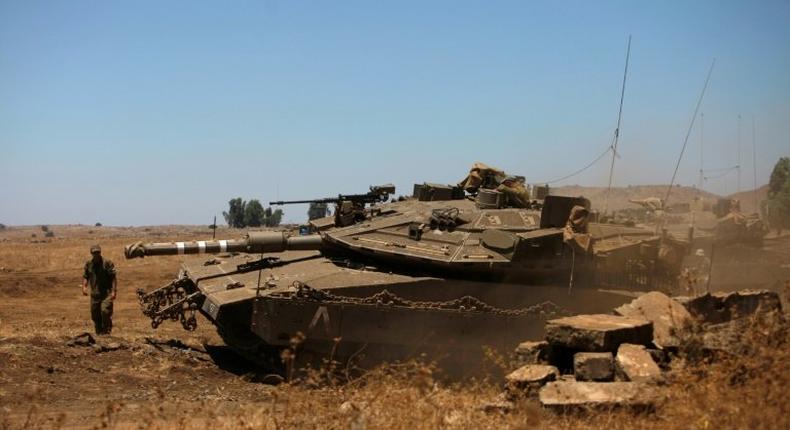 An Israeli soldier directs a Merkava tank stationed in the Israeli-annexed Golan Heights near the Quneitra crossing with Syria