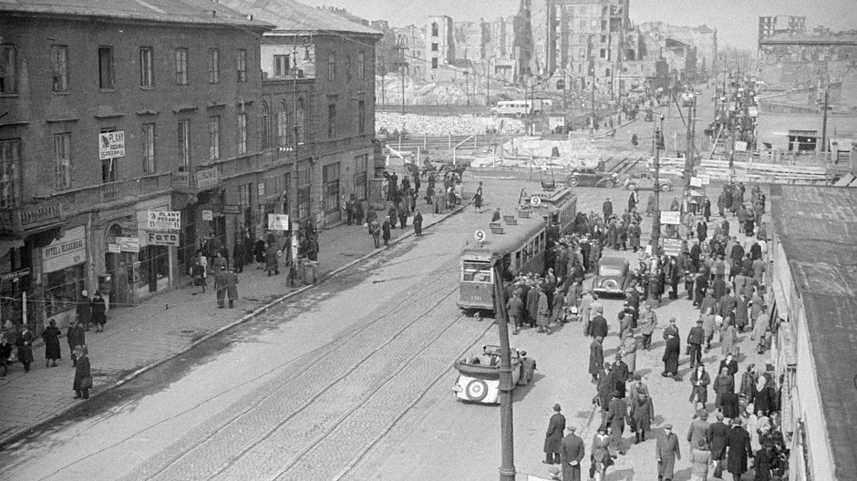 Warszawa. Widok w kierunku północnym. Widoczny tramwaj linii 9, parterowe pawilony i sklepy w przyziemiu willi Marconiego przy al. Jerozolimskich 35 róg ul. Marszałkowskiej 101. W tle przebudowa torów tramwajowych w Al. Jerozolimskich i na horyzoncie ruiny kamienic przy ul. Chmielnej, 1947 r.