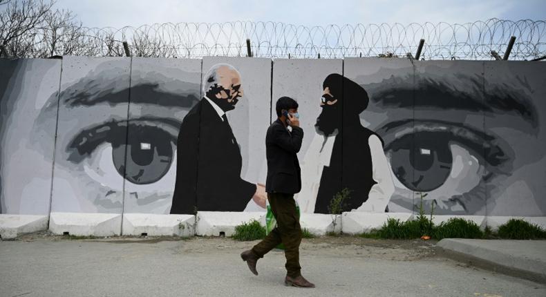 A man wearing a facemask walks past a mural in Kabul depicting the troop withdrawal agreement signed by US Special Representative Zalmay Khalilzad and Taliban co-founder Mullah Abdul Ghani Baradar