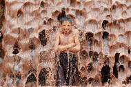An Afghan boy cools off under a muddy waterfall on the outskirts of Jalalabad province