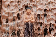 An Afghan boy cools off under a muddy waterfall on the outskirts of Jalalabad province