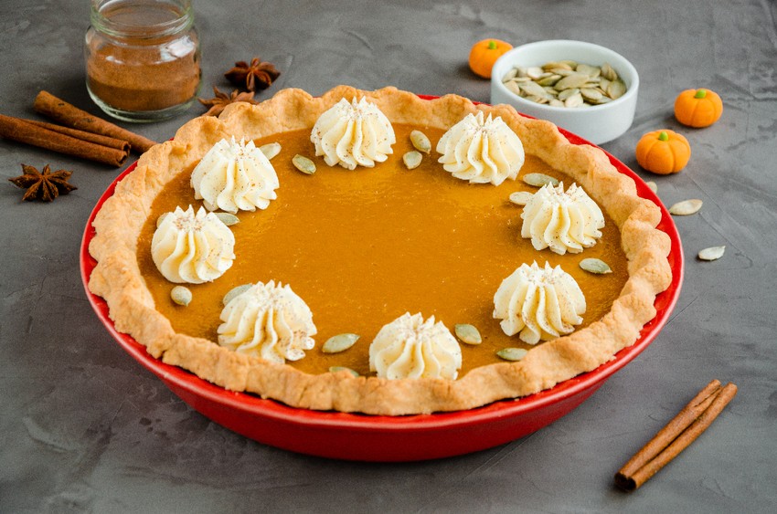 Traditional festive pumpkin pie with spices, whipped cream and seeds on top on a dark stone background. Dessert for Thanksgiving.