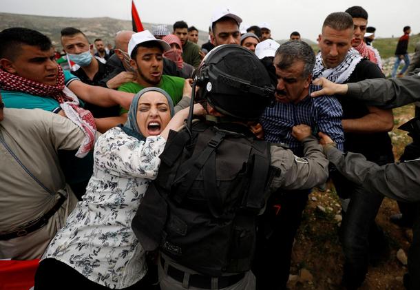 Palestinians try to prevent Israeli troops from detaining a protester during a protest marking Land 