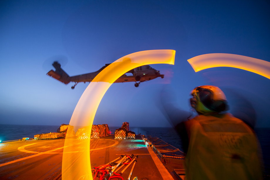 Boatswain's Mate Seaman Clayton Jackson, from Minneapolis, guides an MH-60S Sea Hawk helicopter assigned to the "Dragon Whales" of Sea Combat Squadron 28 during a night vertical replenishment aboard the guided-missile cruiser USS Philippine Sea.