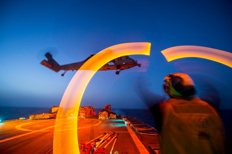 Boatswain's Mate Seaman Clayton Jackson, from Minneapolis, guides an MH-60S Sea Hawk helicopter assigned to the "Dragon Whales" of Sea Combat Squadron 28 during a night vertical replenishment aboard the guided-missile cruiser USS Philippine Sea.