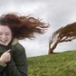 Young woman standing on windswept hill, smiling, eyes closed