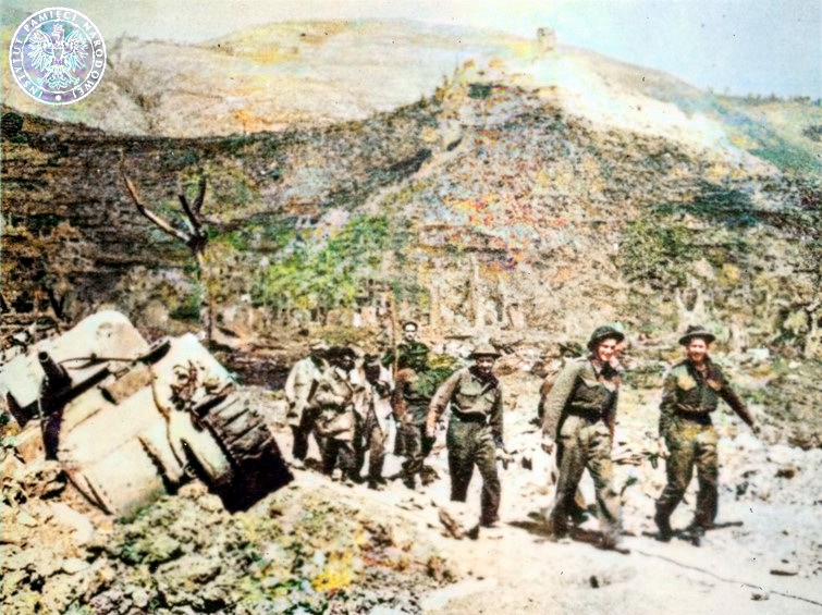 Polscy żołnierze niosą i prowadzą rannych. Na drugim planie klasztor na Monte Cassino. Po lewej stronie: zniszczony czołg M4 Sherman.