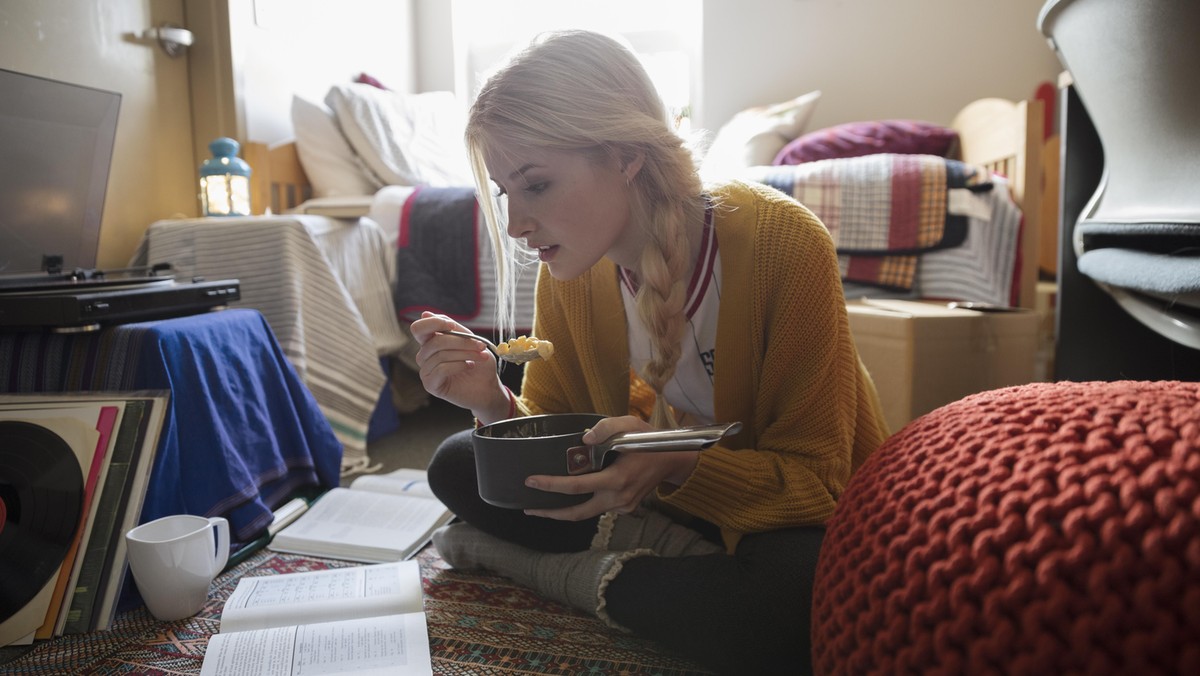 Female college student eating and studying on floor in dorm room