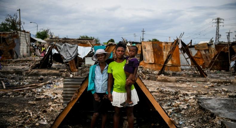 Iris Daniel, 57, Lovely Saint-Pierre, 32, and Evanston Daniel, 5, pose on May 25, 2019, outside a makeshift shelter on the site of their home which was burned during a November 2018 gang war in Port-au-Prince